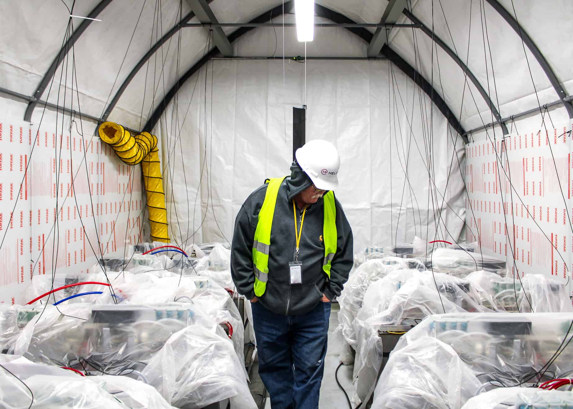 أحد العاملين في هيليون يرتدي خوذة ويسير في ممر محاط بآلات مغطاة بشرائح من البلاستيك